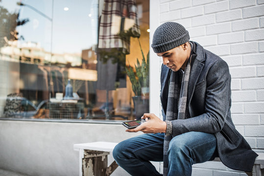 Fashionable young man texting on bench 