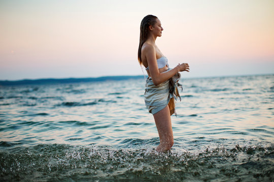 Young woman standing in sea at sunset 