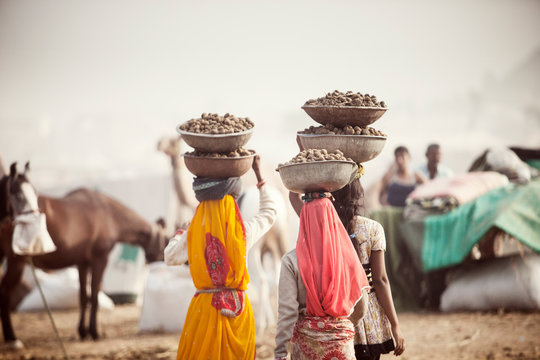 Women transporting food in large bowls balanced on heads at Pushkar Camel Festival 