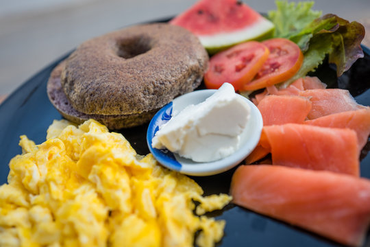 Deep purple rice begel with fried egg and salad in black plate.