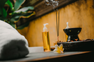 Outdoor spa salon. Massage oils, burning incense sticks with smoke, towels, flowers on wooden  stone table. Bath, green leaves on background