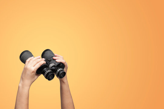 Hands holding binoculars on yellow background