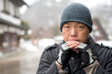 The Asian guy with snow hat stare into the camera and thinking something, Shirakawako valley in the snow season background.