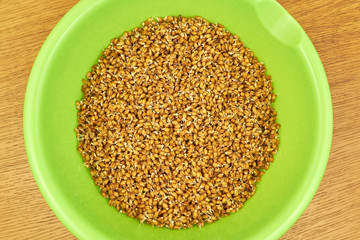 young seeds of sprouted wheat in a bright green deep plate on a wooden table. view from above
