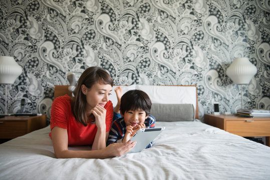 Smiling mother and son using digital tablet on bed at home