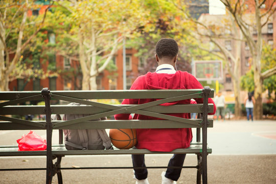 Teenager sitting on bench near basketball field 