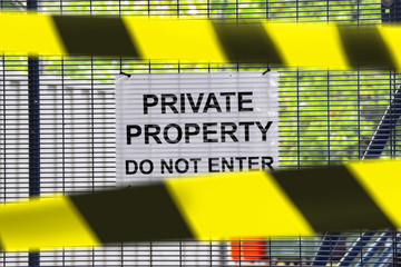 Sign on the fence of the construction site with the inscription PRIVAT PROPERTY DO NOT ENTER closed with prohibitory tapes