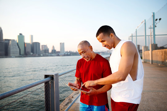 Two men using digital tablet cityscape in background 