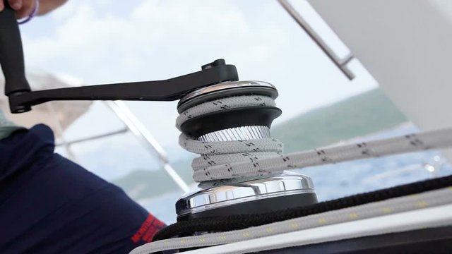 Sailor ties rope on handling appliance. Hands pulling ropes, winding sheets around winches close-up. Sailor's hand on a winch of sailing boat. Sailing.