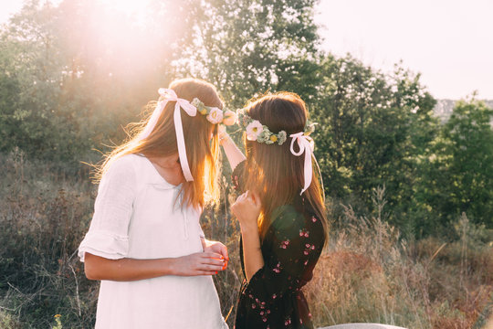 Two young girls hug during sunset in the field with wine glasses friendship concept copy space