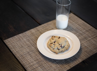 Delicious chocolate chip cookie on a plate and a glass of milk sitting on a table