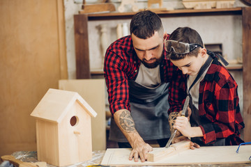 Young caucasian father and his pre-teen son working together in a wooden workshop, building a...
