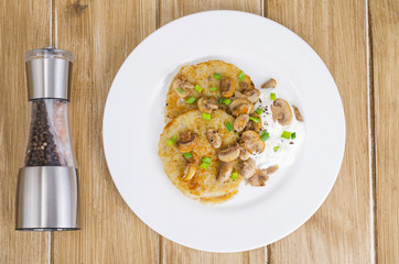 Rustic food concept. Fried potato pancakes with sauce and mushrooms on wooden table