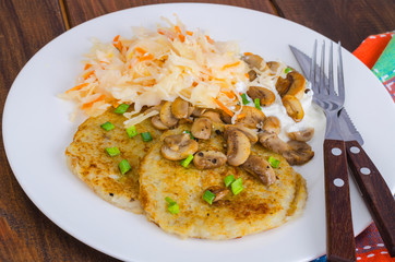 Rustic food concept. Fried potato pancakes with sauce and mushrooms on wooden table