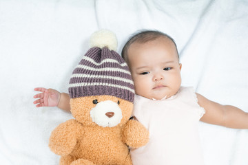 Asian newborn baby hug her brown bear doll wearing knitting hat on white background