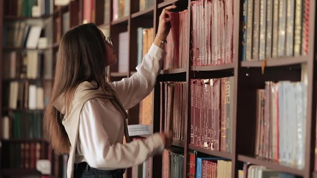 Girl in glasses looking for book in library of university