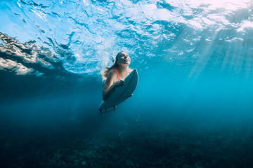 Surfer girl with surfboard dive underwater