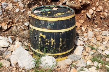 Wooden vine barrel with cracked boards and faded color left in backyard surrounded with stones and...