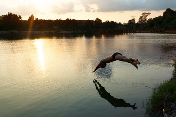 Fototapeta premium jumping man to swim in calm summer lake water at sunset travel background