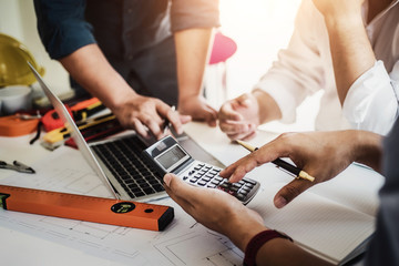 Close up hand of civil engineer or architect business useing calculator about calculate the cost with  for working building plan design project in office.