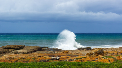 wave crashing againsgt a rock with multi coloured ocean and rocks