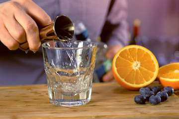 Barman pours the tequila from jigger to rocks glass preparing alcohol cocktail. Hands close-up.