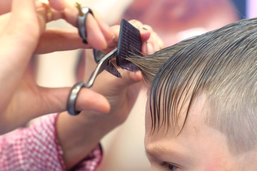 Hairdresser cuts bangs with scissors on boy's head. Stylist's hands close-up, side view.
