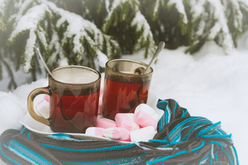 Obraz na płótnie Canvas Two cups of tea with marshmallows under the tree in winter in the snow