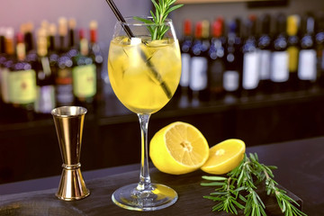 Alcohol cocktail with sparkling wine, ice and liquor , lemon and rosemary in wineglass on bar...