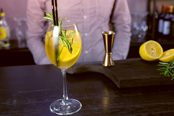 Alcohol cocktail with sparkling wine, ice and liquor , lemon and rosemary in wineglass on bar...