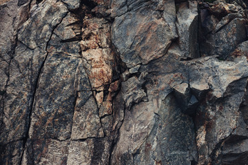 Fragment of a rock in the mountains, destroyed in cracks close-up, dark and brown