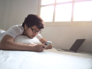 Relaxed Asian man with mobile smart phone lying down on the bed in morning