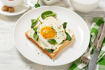 Toast with cream cheese, spinach and fried egg, top view.