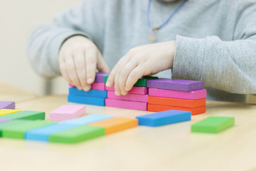 Child playing with building blocks learning new skills.a hand is putting last cube on the top of pyramide