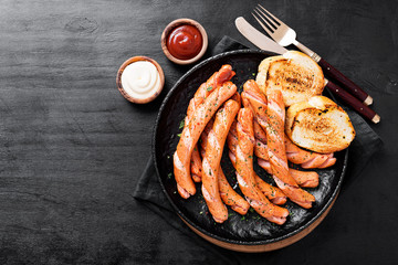 Grilled sausages and different sauce on a dark wooden background.