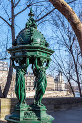 Fototapeta premium Parisian drinking fountain with Seine river and palace of justice in background - Paris, France