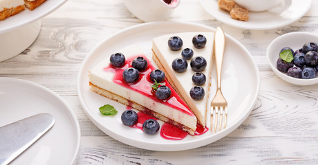 Cheesecake with fresh blueberry and berry sauce on white wooden table. © Nelea Reazanteva