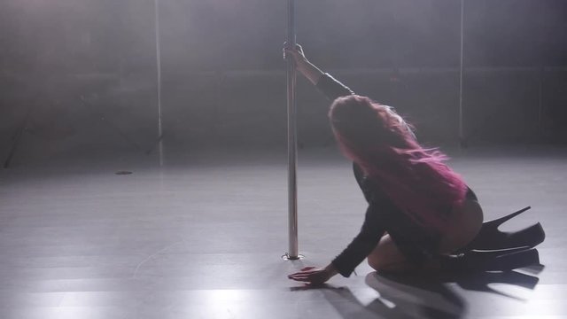 Concept of dance and acrobatics. Young slim woman pole dancing in dark interior with backlight and smoke