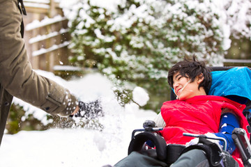 Disabled boy in wheelchair playing in winter snow