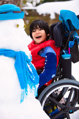 Happy smiling disabled boy in wheelchair building a snowman