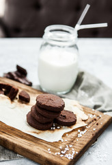 A stack of chocolate cookies with milk on a wooden board