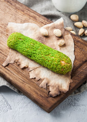 Delicious pistachio green eclair on a wooden board with a bottle of milk