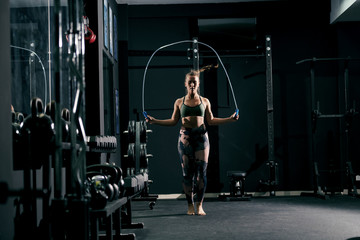 Fototapeta na wymiar Strong caucasian boxer girl in sportswear jumping rope in gym.