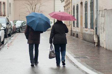 portrait of couple  walking with colorful umbrellas in the street on back view