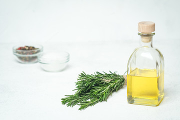 Fresh rosemary herb with oil and spices on a light background.