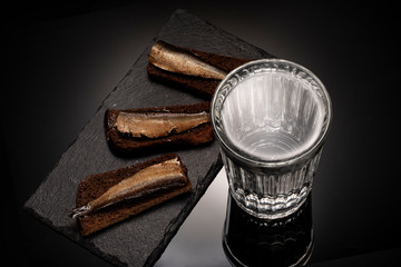 Glass with vodka and appetizer with sprat and bread.