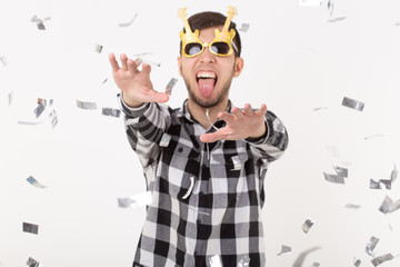 people, holidays and party concept - young man in glasses dancing in confetti on white background