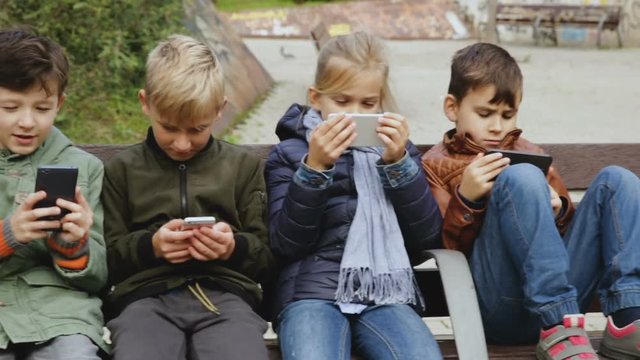 Group of preteen children sitting on bench outdoors, addicted in their phones