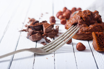 broken chocolate muffin and hazelnuts, fork on white wood table
