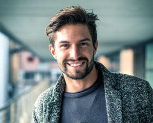 One handsome young man in urban setting in European city, standing and smiling to camera happy